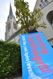 Die Pfarrer Markus Keller und Lukas Butscher entrollen die neue Blache vor der Kirche. (Bild: Manuel Nagel)