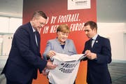Die deutsche Kanzlerin Angela Merkel erhält anlässlich der deutschen Kandidatur für die EM 2024 von DFB Präsident Reinhard Grindel (links) und Ex-Nationalspieler Philipp Lahm ein Trikot überreicht. (Bild Felix Zahn/Bundesregierung via Getty Images (Berlin, 27. März 2018)))