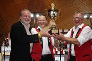 Martin Sebastian von Alpenrosen überreicht Präsident Karl Thoma und Dirigent Rolf Gmür (v.l.) den Pokal als Preis für die beliebteste Blaskapelle der Schweiz. (Bild: Trudi Krieg)