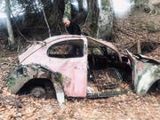 Uli Mack begutachtet das VW-Brezelkäfer-Wrack im Bündner Wald. (Bild: PD)