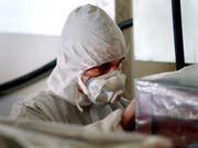 Ein Arbeiter mit Mundschutz und Schutzkleidung bereitet eine Abfallkiste voll asbestverseuchtem Material auf ihren Abtransport vor. (Bild: KEYSTONE/EDDY RISCH)