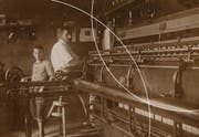 Fotograf unbekannt (ca. 1900-1915). Heimsticker am Pantograph der Handstickmaschine und Knabe an Fädelmaschine im Sticklokal. In Schweizerisches Landesmuseum. (Bild: PD)