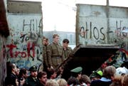 Nach 28 Jahren der Trennung begannen die Berliner nach der Grenzöffnung am 9. November 1989, die Mauer zu demontieren. Ehemalige DDR-Grenzsoldaten schauen ihnen belustigt zu. (Bild: Lionel Cironneau/Keystone (11. November 1989))