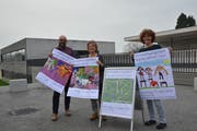 Die Lehrkräfte Sascha Edelmann, Barbara Keller und Maya Perroulaz (von links) mit den von den Schülerinnen und Schülern gestalteten Plakaten, die zur Einweihungsfeier des Erweiterungsbaus (hinten) der HPS in Flawil einladen. (Bild: Zita Meienhofer)