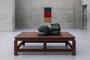 Vorne eine weitere Frauenskulptur auf dem dazugehörigen Stahlpodest, im Hintergrund eine Keramikflagge in verschmutzem Rot-Schwarz-Gold. (Bild: Markus Tretter)
