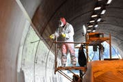 Gut geschützt bringt ein Arbeiter die Spezialfarbe an den Wänden im Aeulitunnel auf. Die helle Farbe reflektiert das Licht und macht so den Tunnel heller. (Bild: Urs M. Hemm)