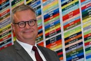 Christoph Kohler posiert in der Schulverwaltung vor der bunten Wand mit all den Namen der Schülerinnen und Schüler, die in Amriswil, Hefenhofen und Sommeri zur Schule gehen. (Bild: Manuel Nagel)