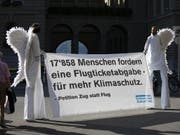 Aktivisten im Engelskostüm tragen am Dienstag ein Banner für die Petition «Ja zur Flugticketabgabe» vor das Bundeshaus. (Bild: Keystone/PETER KLAUNZER)