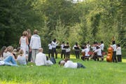 Idylle mit falschem Unterton bei der Performance von Sislej Xhafa: Das Argovia Philharmonic spielt in lauschiger Natur, sieht mit seinen Sturmmasken aber aus wie Schwerverbrecher. (Bild: Alex Spichale,31.8.2019)