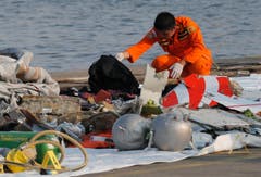 Ein Mitarbeiter der Rettungsdienste untersucht Trümmerteile. (Bild: AP Photo/Tatan Syuflana)