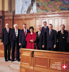 1999, Bild 1 (von links): Pascal Couchepin, Flavio Cotti, Adolf Ogi, Bundespräsidentin Ruth Dreifuss, Arnold Koller, Bundeskanzler François Couchepin, Kaspar Villiger, Moritz Leuenberger.