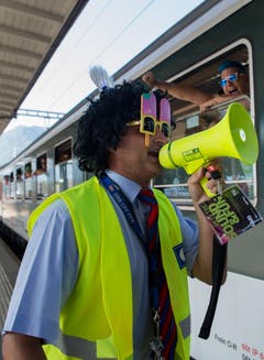 Ein mit Perücke und Brille verkleideter Zugführer der SBB gibt das Abfahrtssignal für den Street-Parade-Extrazug von Lugano nach Zürich. (Bild: Keystone)