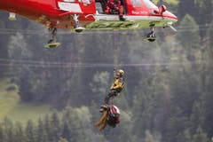 Ein Rega-Helikopter fliegt einen Retter und Bergungsmaterial vom Unglücksort im Beriech der Kirche St. Peter Mistail zum Umladeplatz in Tiefencastel. (Bild: Keystone)