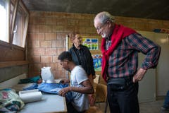 Besucher Oskar Stockmann interessiert sich für einen jungen Asylsuchenden, der Hosen an der Nähmaschine flickt. Begegnungs- und Gestaltungsraum können Asylsuchende unter anderem Zeichnen, Schneidern oder sich gegenseitig die Haare schneiden. (Bild: Dominik Wunderli)