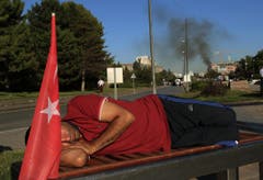 Ein Demonstrant schläft vor dem rauchenden Militärhauptquartier in Ankara. (Bild: AP Photo/Ali Unal)