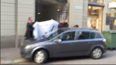 Für die Öffentlichkeit begann die Justiz-Aktion so: Eine Person mit Geleitschutz wird in einen wartenden Wagen geführt. Das Bild stammt von einem Handyvideo vom Mittwoch und wurde am Seiteneingang des Hotels Baur au Lac aufgenommen. (Bild: AP Photo / Rob Harris)