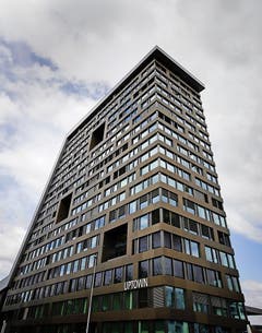 Uptown, Zug Der Standort rechtfertigt sich mehr aus der Quersubventionierung des Eishockeystadions als auf Grund städtebaulicher Notwendigkeit. Eine öffentliche Nutzung ergibt sich durch ein Restaurant im Erdgeschoss und ein weiteres im Dachgeschoss - wo man auch als nicht zahlender Gast die Aussicht geniessen kann. Die ungewöhnliche Scheibenform wirkt in der Ferne problematisch. Die Fassade gegen Norden mit Dachfenstern als Öffnung wirkt fremd. (Bild: Stefan Kaiser / Neue ZZ)