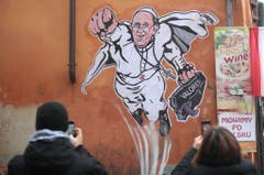 Ein auf einer Hausmauer in Rom angebrachter Wandsticker zeigt Papst Franziskus als Superhelden und ist bei Passanten ein beliebtes Fotomotiv. (Bild: Keystone)