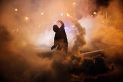 Ein Protestierender wirft eine rauchende Petarde zurück. (Bild: AP Photo / David Goldman)