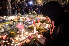 Eine Frau zünden eine Kerze an. (Bild: EPA/CHRISTOPHE PETIT TESSON)
