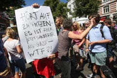 Teilnehmer diskutieren mit anderen, die von der Putzaktion nicht so begeistert scheinen. Eine von Ihnen hält dabei ein Transparent mit der Aufschrift "Hört auf zu putzen - Es ist hier jetzt sauberer als sonst - wtf?! (What the fuck?!)". (Bild: KEYSTONE/DPA/A3833/_Bodo Marks)