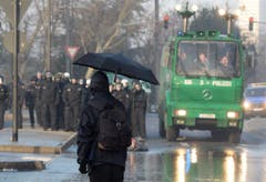 Ein maskierter Demonstrant mit einem Regenschirm steht Polizisten gegenüber. (Bild: Keystone)