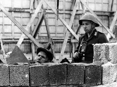 Unter der Bewachung eines DDR-Grenzpolizisten beseitigen Bauarbeiter am 26. Mai 1962 Sprengstoffschäden an der Berliner Mauer in der Bernauer Strasse/Ecke Schwedter Strasse. Eine Explosion kurz nach Mitternacht hatte ein zwei Meter breites Loch in die Mauer gerissen. (Bild: Keystone)