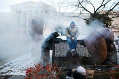 Obdachlose wärmen sich an einem Dampfabzug der Staatlichen Handelsbehörde in Washington. (Bild: Keystone)