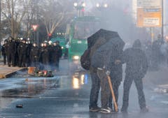 Maskierte Demonstranten schützen sich mit einem Schirm vor den Wasserkanonen der Polizei. (Bild: Keystone)
