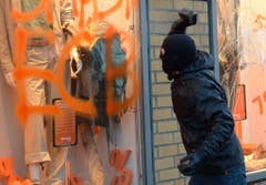 Ein Demonstrant wirft einen Stein in ein verspraytes Schaufenster in Frankfurt. (Bild: Keystone)