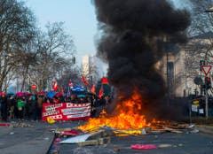 Protestierende mit Fähnchen und einem Plakat hinter brennenden Barrieren. (Bild: Keystone)