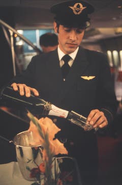Champagner gefällig? Ein Steward in der First Class einer frühen 747 der Swissair. Im Hintergrund ist die Wendeltreppe sichtbar, die zur Lounge auf dem Oberdeck führte. (Bild: ETH-Bibliothek/Bildarchiv/Stiftung Luftbild Schweiz/Swissair)