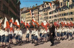 Eine Bubenklasse mit ihren Schulfahnen auf einer kolorierten Ansichtskarte um 1932.