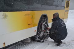 Der Chauffeur montiert in Wildhaus Dorf Schneeketten auf das Doppelstock-Postauto.(Bild: Adi Lippuner)