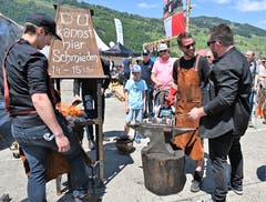 Schmiedemeister Yannick Christen von der Kreativen Metallgestaltung Dallenwil (links) zeigt dem Besucher Efrem Zimmermann (Mitte) wie man mit Hammer, Amboss und 900 Grad Hitze umgeht! (Bild: Romano Cuonz, Buochs, 30.Mai.2019)