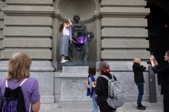 Eine Aktivistin hängt eine Fahne an eine Statue vor dem Bundeshaus. (Bild: KEYSTONE/Peter Klaunzer)