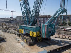 Ein Blick auf den Sockel des Krans und den Zug im Hintergrund verdeutlicht die gewaltigen Ausmasse der Maschine. (Bild: Keystone/JEAN-CHRISTOPHE BOTT)