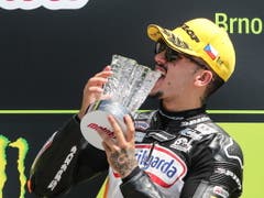 Aron Canter beisst in den Moto3-Siegespokal und freut sich über die WM-Führung (Bild: KEYSTONE/EPA/MARTIN DIVISEK)
